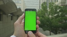 Personal perspective of a businessman holding a smartphone with a green screen