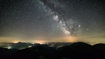 Starry night in mountains time-lapse. Milky way galaxy stars moving over countryside traffic. Night to day
