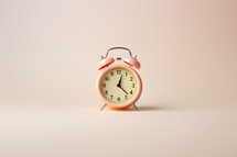 A pink retro looking alarm clock on a pink background