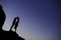 silhouette of an expecting couple standing at the edge of a cliff 