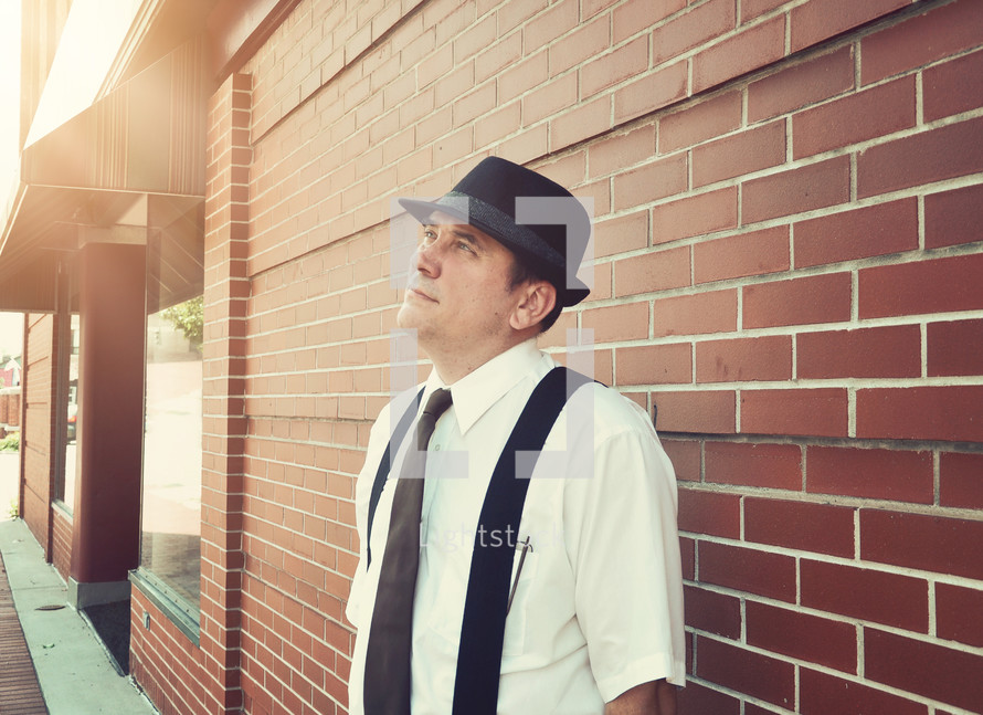 a man in a hat and suspenders looking up to God 