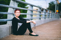 A woman sitting against the railings on an overpass. 