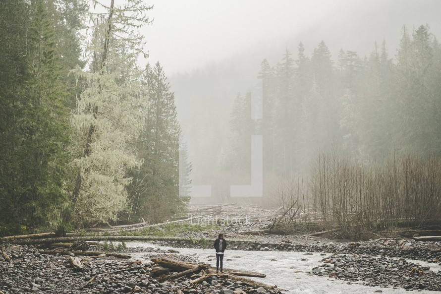 a man standing by a river in fog 
