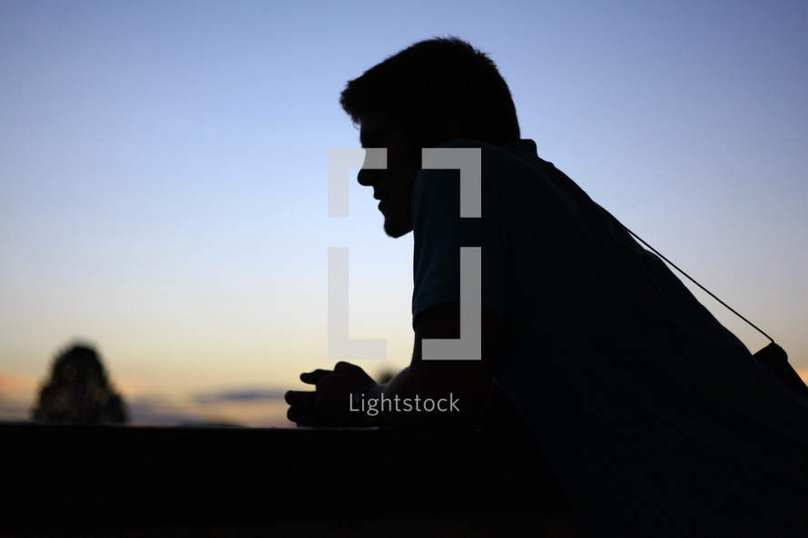 Man leaning on wall at sunset