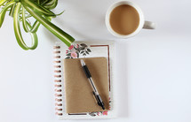journal, pen, houseplant, and coffee cup on a desk 