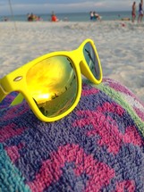 Yellow sunglasses on a beach towel at the beach.