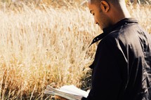 man reading a Bible in a field 