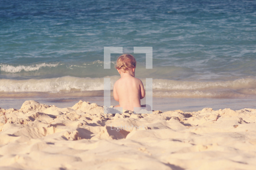 naked toddler sitting on a beach 