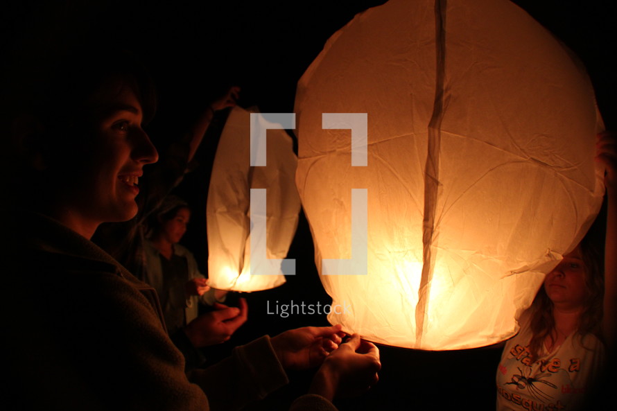 friends lighting floating paper lanterns at night 