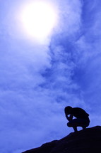 Silhouette of a man kneeling in prayer at the top of a mountain 