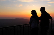 Silhouette of a man and woman looking out toward the sunset.
