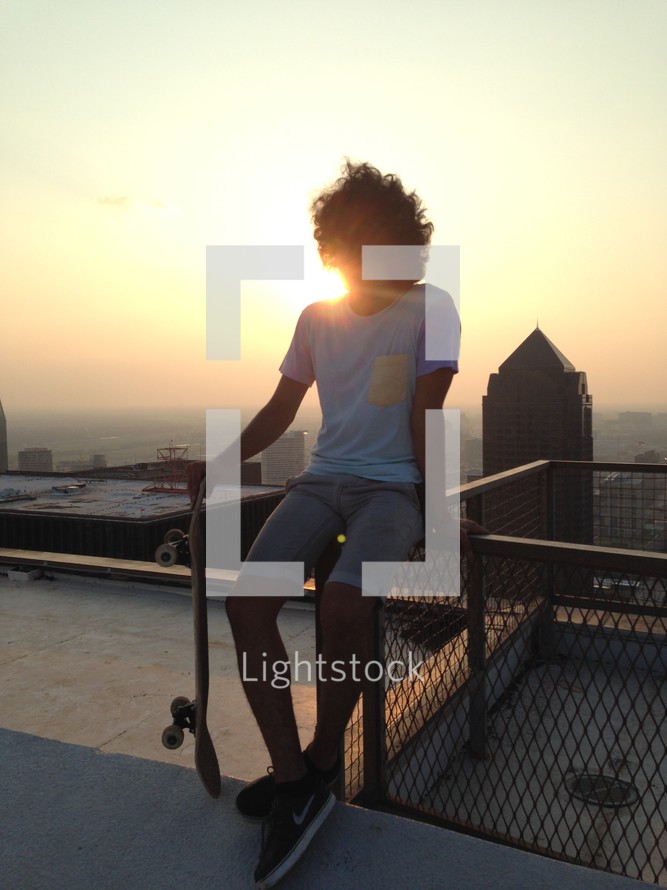 young man with a skateboard on a rooftop in a city 