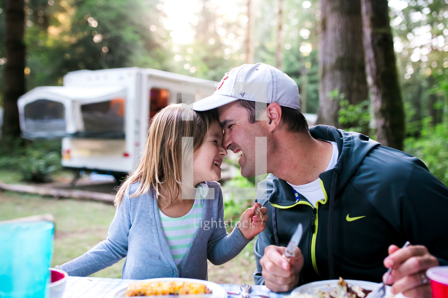 a father and daughter eating outdoors at a picnic table next to an RV