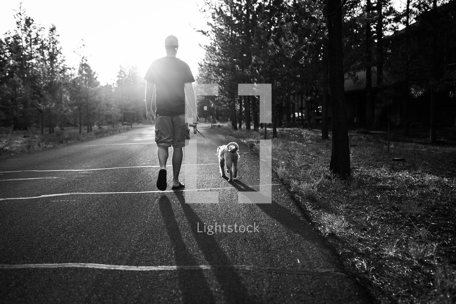a man walking his dog on a leash at sunset 