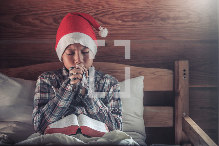 a boy in a Santa hat reading a Bible and praying 