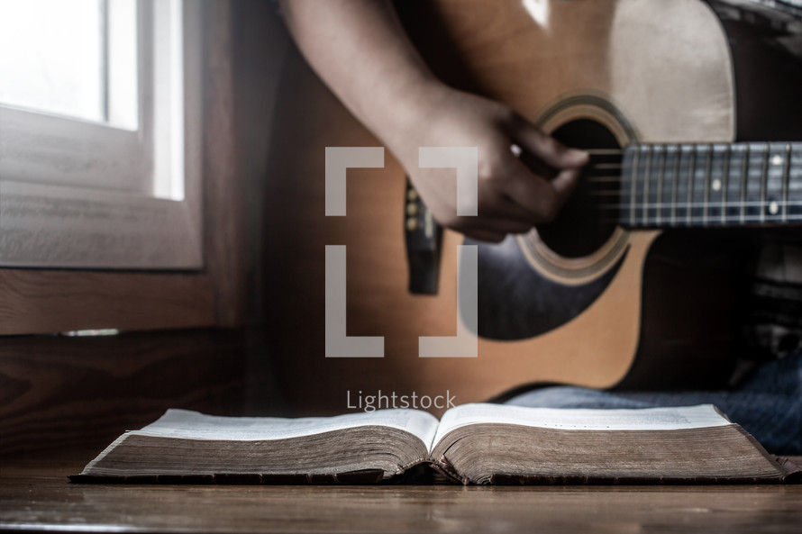 a person playing a guitar next to an open Bible 