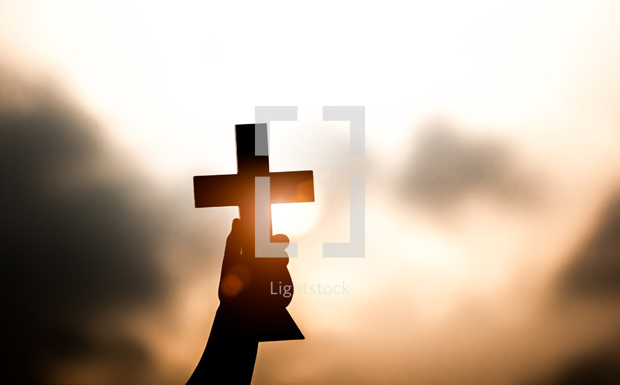 young man holding up a cross at sunset 