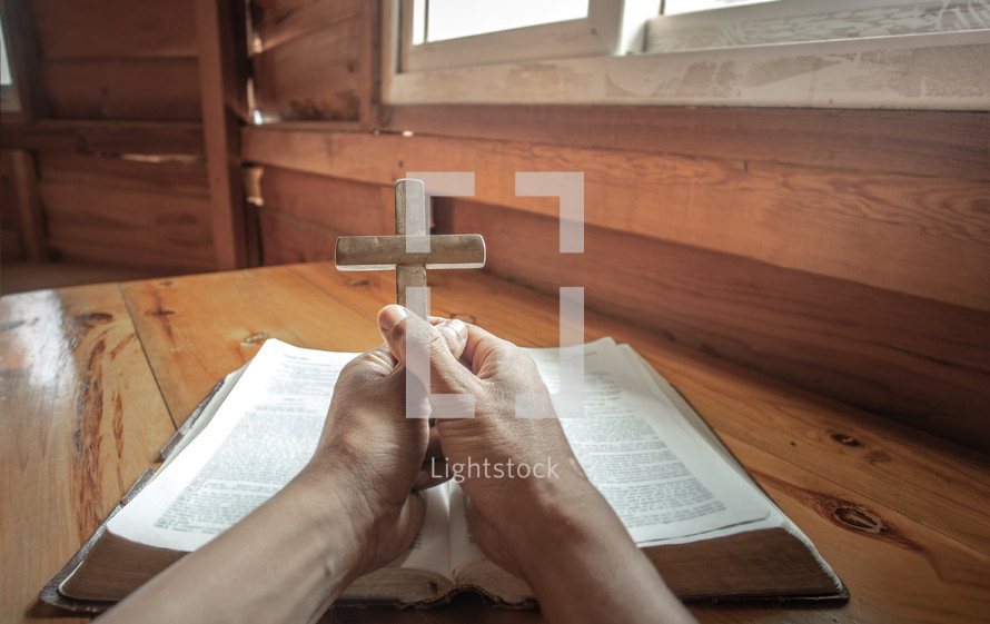 hands holding a wooden cross over a Bible 