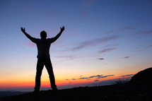 silhouette of a man with raised hands against the rising sun