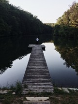 man standing at the end of a dock on a pond 