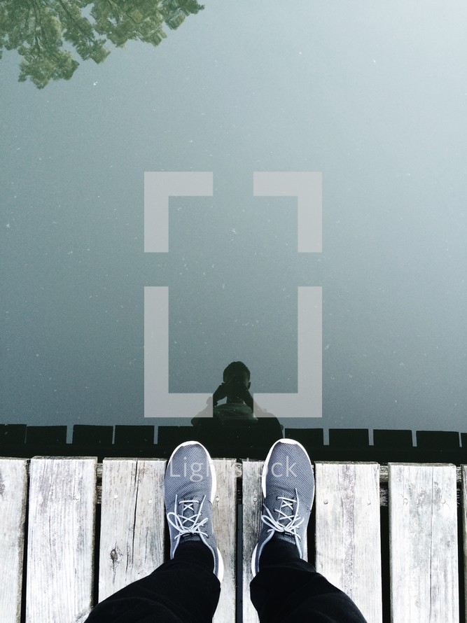reflection of a man standing on a dock in lake water 