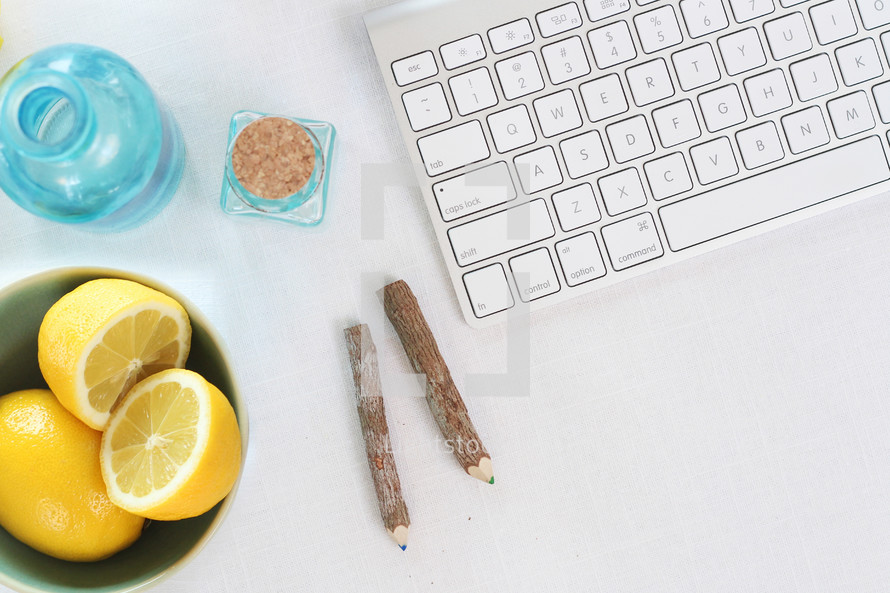 keyboard, bowl of lemons, pencils, bottles on a desk 