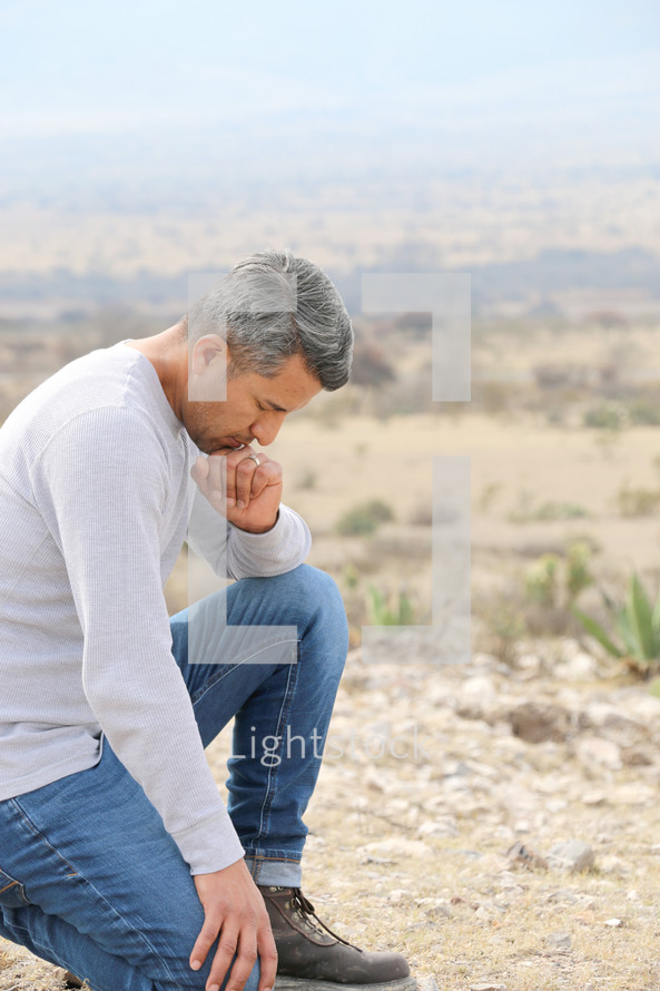 a man kneeling in prayer in a desert