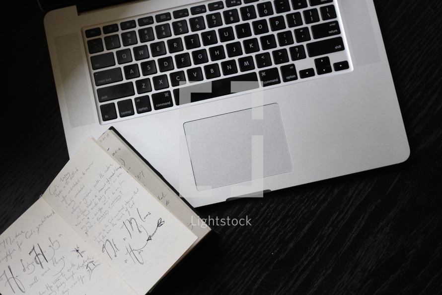 notes in a journal and keyboard on a laptop 