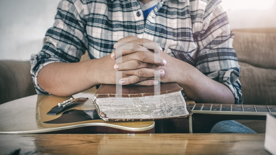praying hands over a Bible on a guitar 