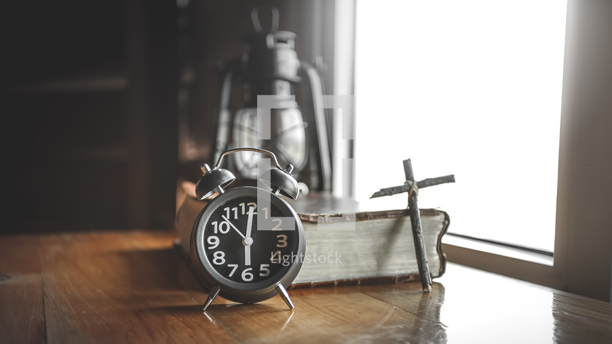 oil lamp, alarm clock, cross, and Bible in a window 