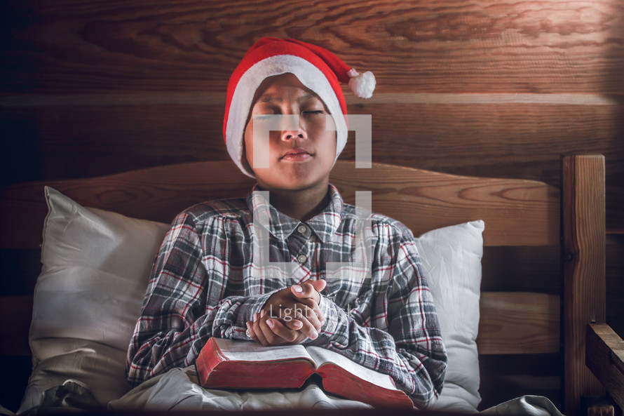 a boy in a Santa hat reading a Bible and praying 
