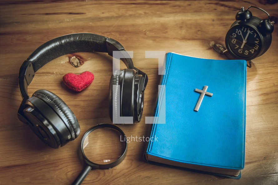 headphones, Bible, alarm clock, and red felt heart on a wooden table 