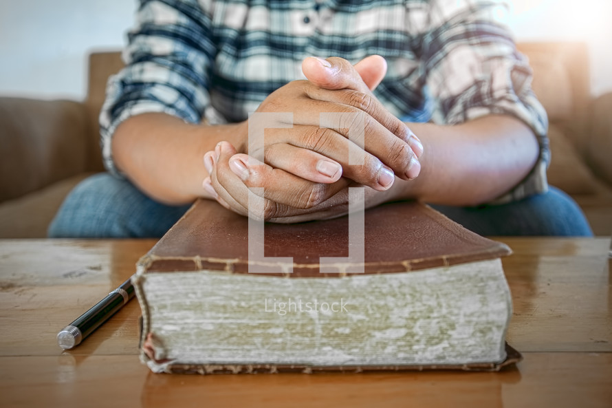 man with praying hands over a closed Bible 