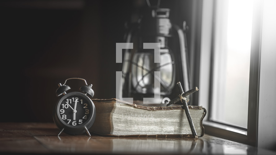oil lamp, cross, and alarm clock near a Bible 