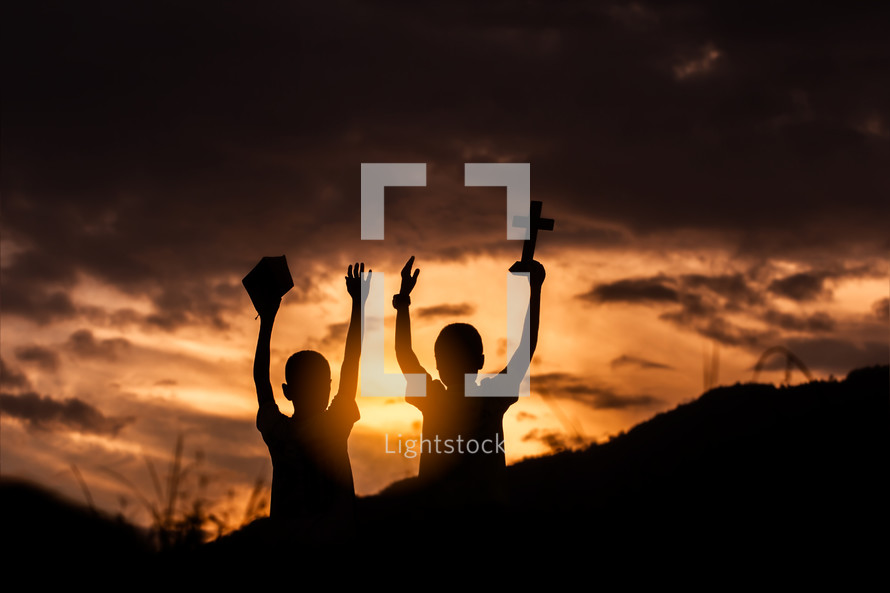 two boys with hands raised at sunset 