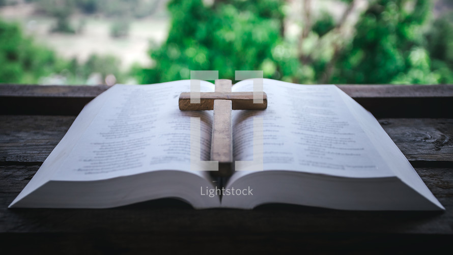 wooden cross on the pages of a Bible in a window 