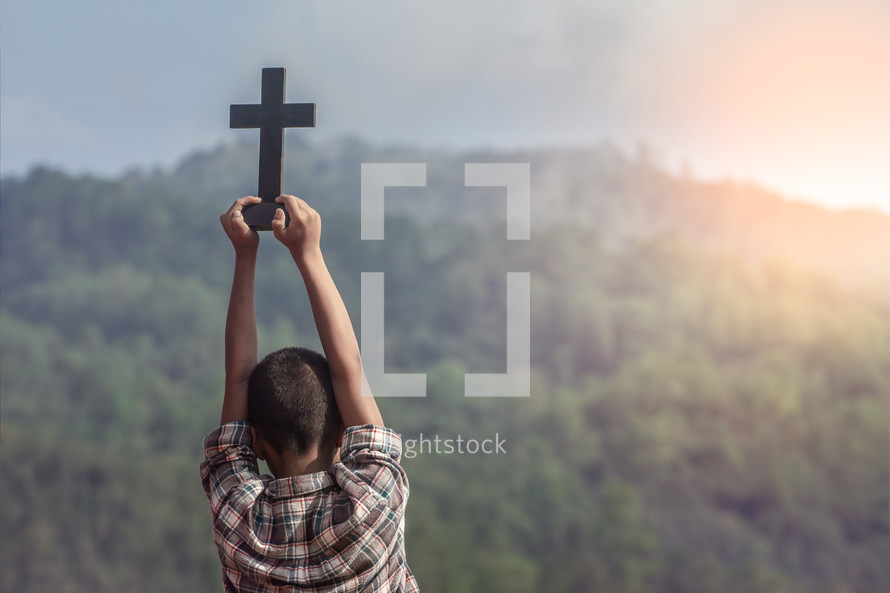 a boy holding up a cross outdoors 