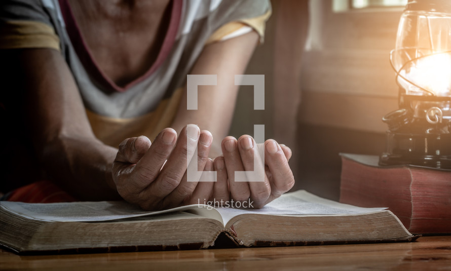 senior woman with hands over a Bible in prayer 