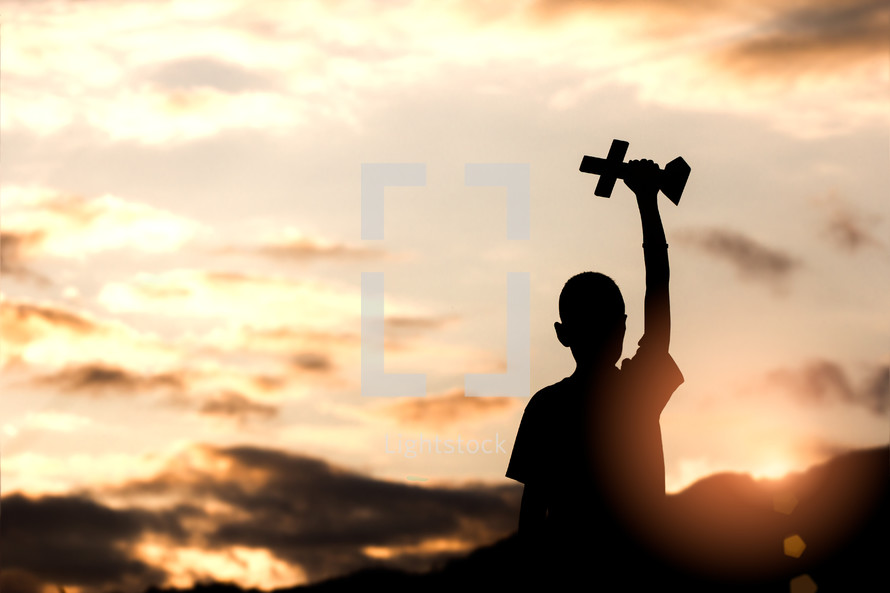 a silhouette of a boy holding a cross at sunrise 
