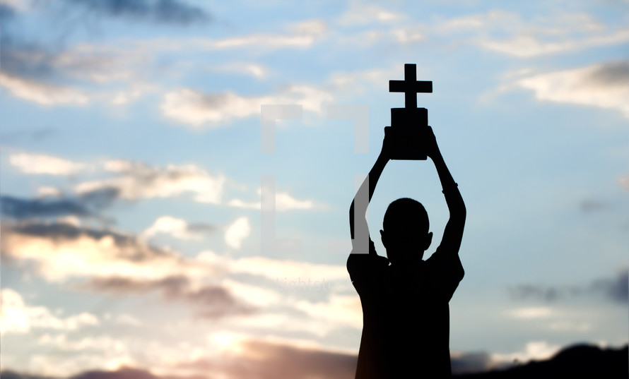 silhouette of a boy holding up a cross 