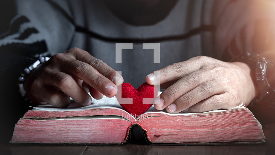 a man holding a red felt heart over a Bible 