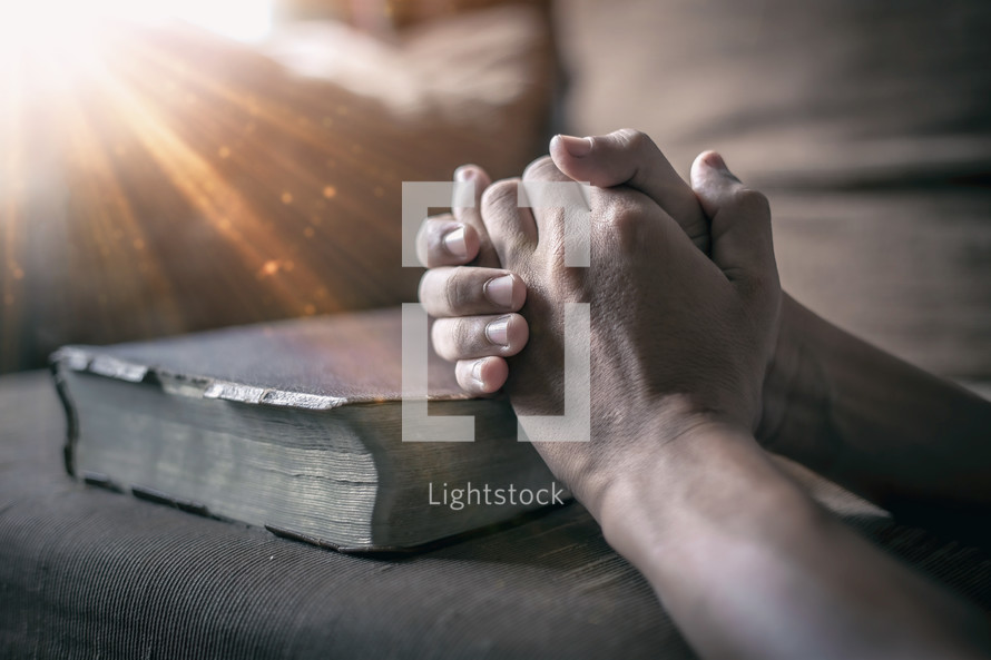 a man's praying hands over a Bible 