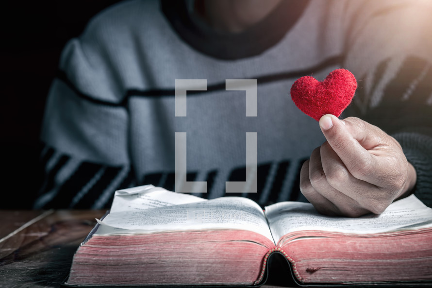 a man holding a red felt heart over the pages of a Bible 