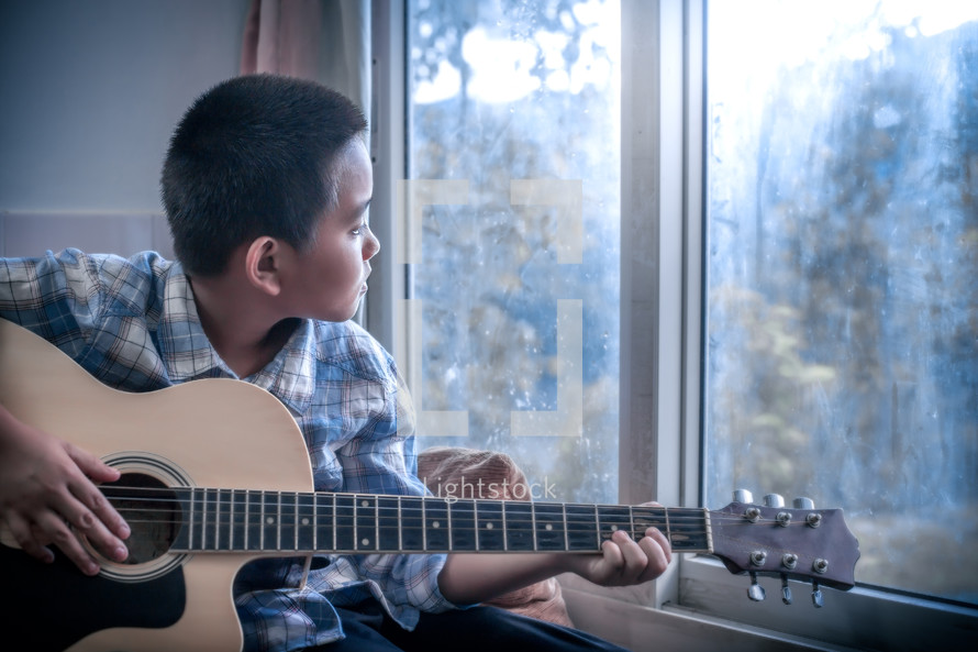 a boy playing a guitar sitting in a window 