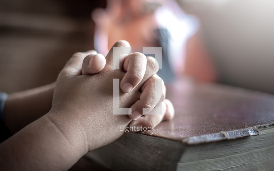 child's praying hands over a Bible 