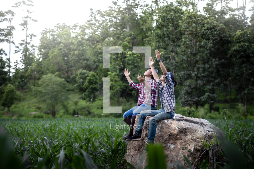 Two young male hands raised and praying in corn field.