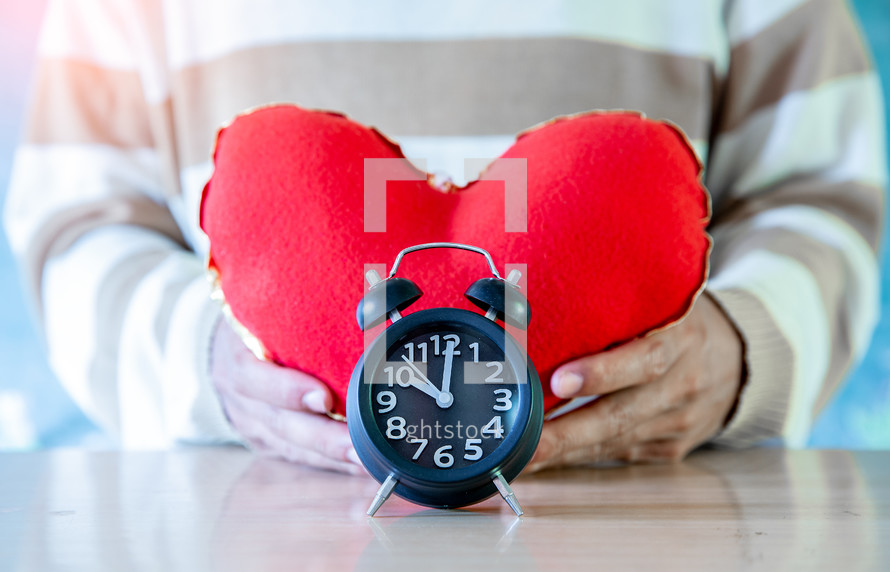 person holding a red heart and alarm clock, valentine day background.