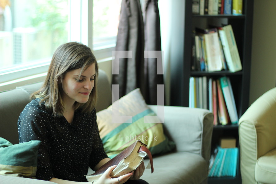 a woman holding a Bible while sitting on a couch 