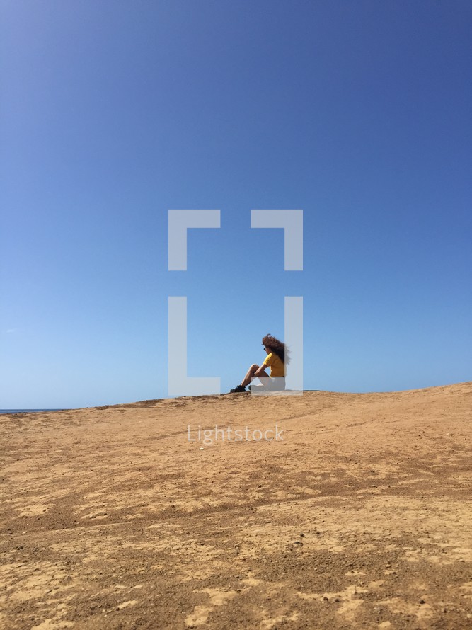 woman sitting at the top of a sand dune 