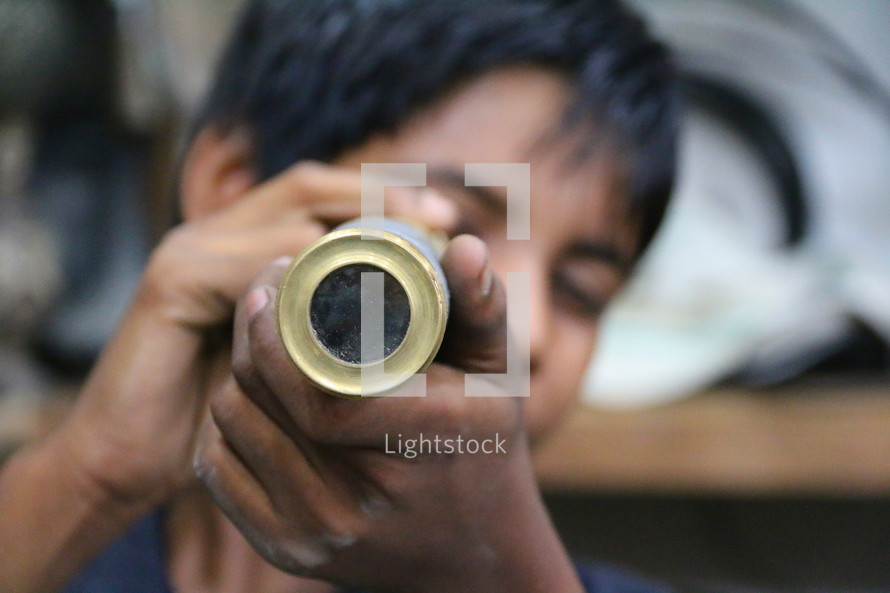 Young boy peers through an old brass telescope